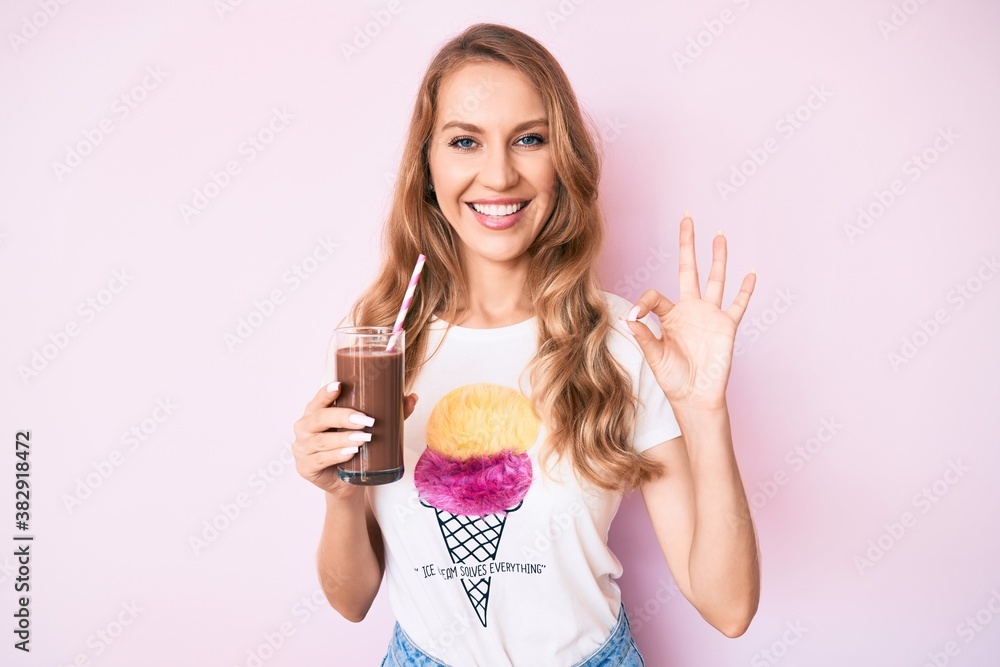 Young caucasian woman with blond hair drinking chocolate milkshake doing ok sign with fingers, smiling friendly gesturing excellent symbol Young caucasian woman with blond hair drinking chocolate milkshake doing ok sign with fingers, smiling friendly gesturing excellent symbol