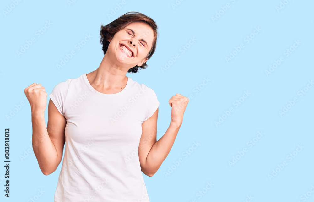 Fototapeta premium Beautiful young woman with short hair wearing casual clothes very happy and excited doing winner gesture with arms raised, smiling and screaming for success. celebration concept.
