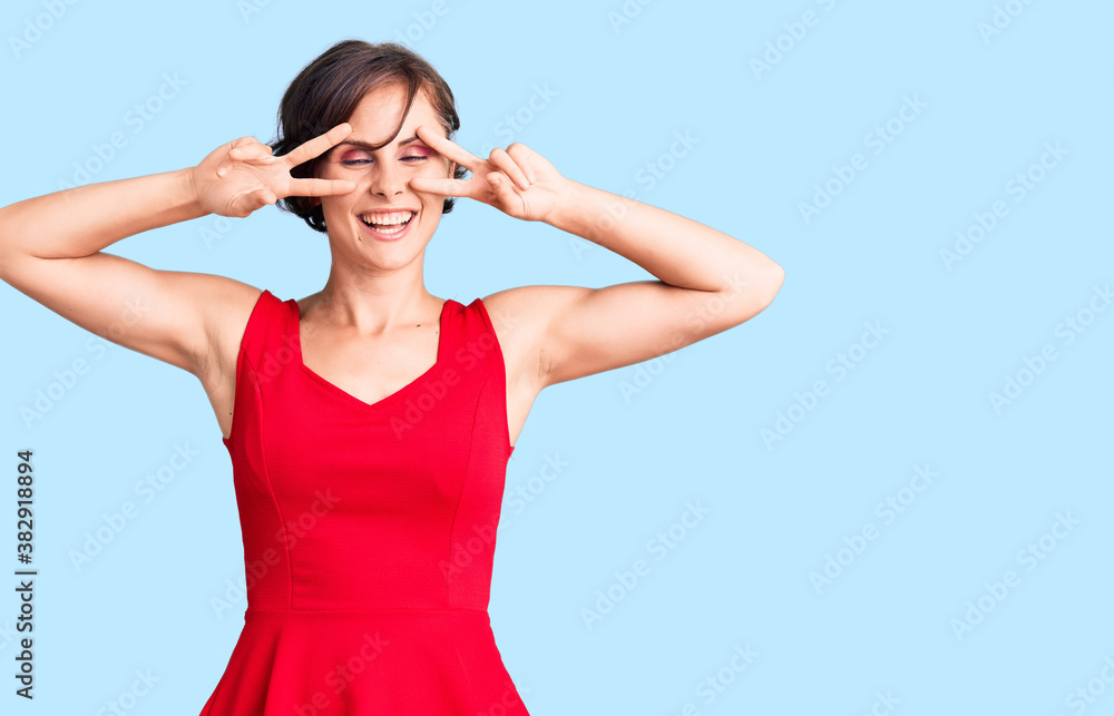 Beautiful young woman with short hair wearing casual style with sleeveless shirt doing peace symbol with fingers over face, smiling cheerful showing victory Beautiful young woman with short hair wearing casual style with sleeveless shirt doing peace symbol with fingers over face, smiling cheerful showing victory