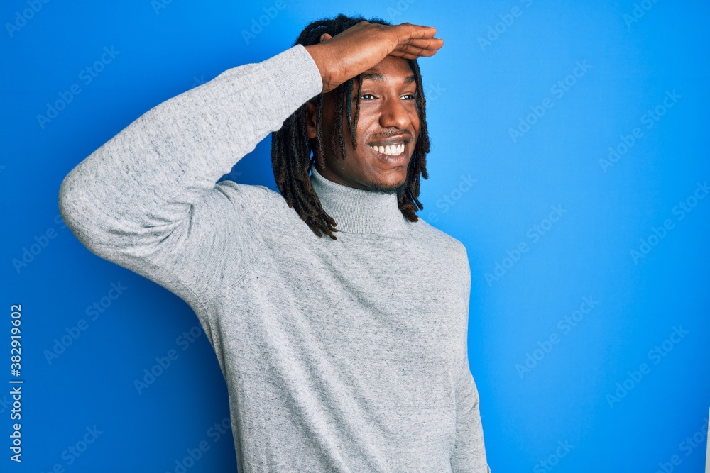 Naklejka premium African american man with braids wearing turtleneck sweater very happy and smiling looking far away with hand over head. searching concept.