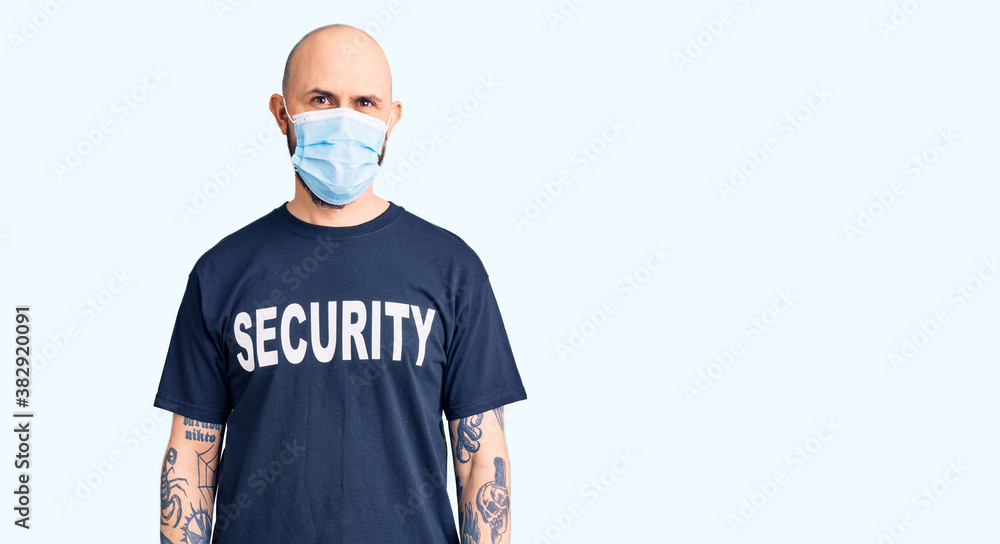 Young handsome man wearing security t shirt and medical mask looking positive and happy standing and smiling with a confident smile showing teeth Young handsome man wearing security t shirt and medical mask looking positive and happy standing and smiling with a confident smile showing teeth