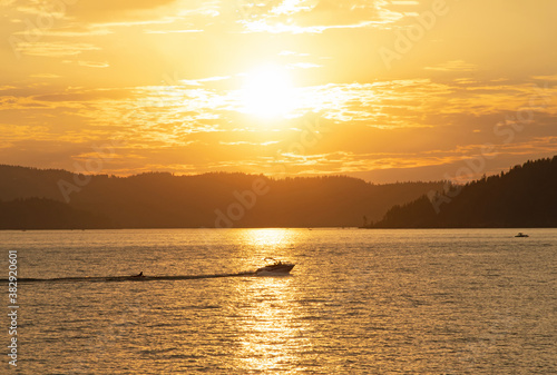 Original sunset photograph of a boat pulling a rafter across the lake at sundown