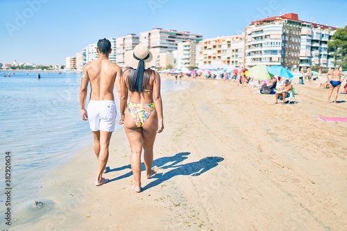 Young latin couple wearing swimwear  walking on back view at the beach. © Krakenimages.com