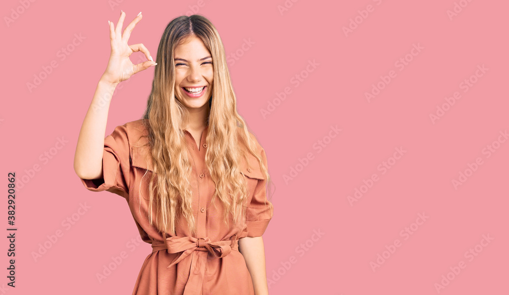 Beautiful caucasian woman with blonde hair wearing summer jumpsuit smiling positive doing ok sign with hand and fingers. successful expression.