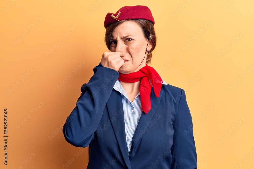 Young beautiful woman wearing stewardess uniform smelling something stinky and disgusting, intolerable smell, holding breath with fingers on nose. bad smell Young beautiful woman wearing stewardess uniform smelling something stinky and disgusting, intolerable smell, holding breath with fingers on nose. bad smell