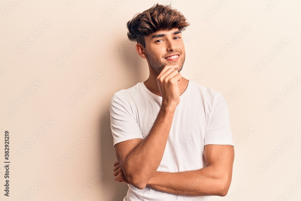 Young hispanic man wearing casual clothes smiling looking confident at the camera with crossed arms and hand on chin. thinking positive. Young hispanic man wearing casual clothes smiling looking confident at the camera with crossed arms and hand on chin. thinking positive.