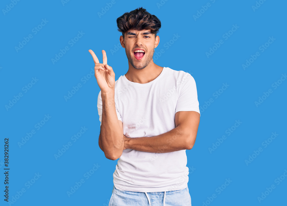 Young hispanic man wearing casual clothes smiling with happy face winking at the camera doing victory sign. number two. Young hispanic man wearing casual clothes smiling with happy face winking at the camera doing victory sign. number two.