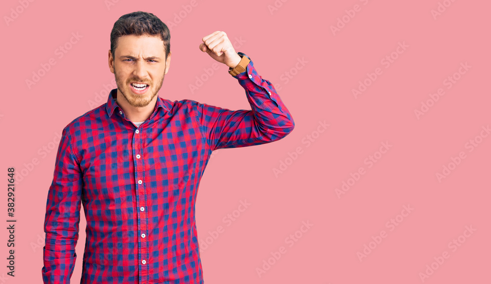 Handsome young man with bear wearing casual shirt angry and mad raising fist frustrated and furious while shouting with anger. rage and aggressive concept. Handsome young man with bear wearing casual shirt angry and mad raising fist frustrated and furious while shouting with anger. rage and aggressive concept.