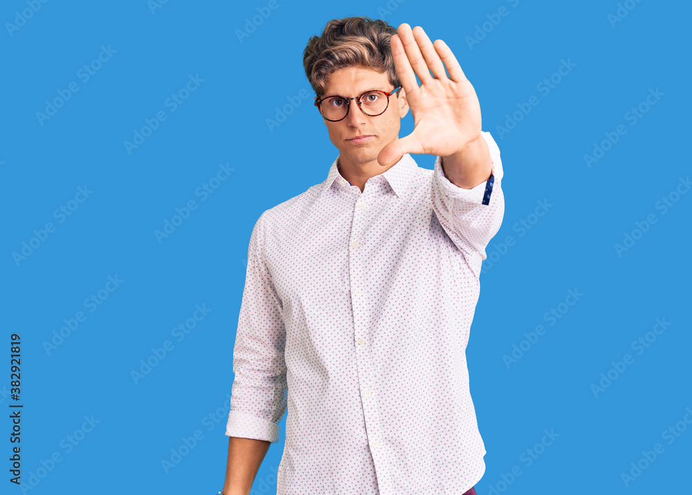 Young handsome man wearing business clothes and glasses doing stop sing with palm of the hand. warning expression with negative and serious gesture on the face. Young handsome man wearing business clothes and glasses doing stop sing with palm of the hand. warning expression with negative and serious gesture on the face.