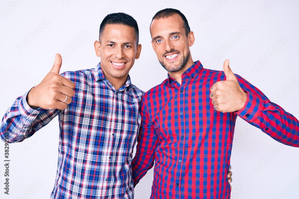 Naklejka premium Young gay couple of two men wearing casual clothes success sign doing positive gesture with hand, thumbs up smiling and happy. cheerful expression and winner gesture.