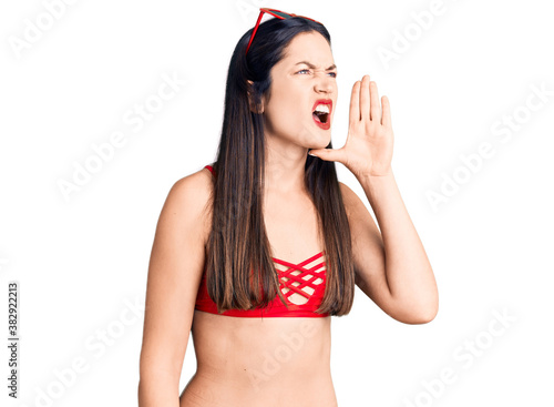 Young beautiful caucasian woman wearing bikini shouting and screaming loud to side with hand on mouth. communication concept. photo