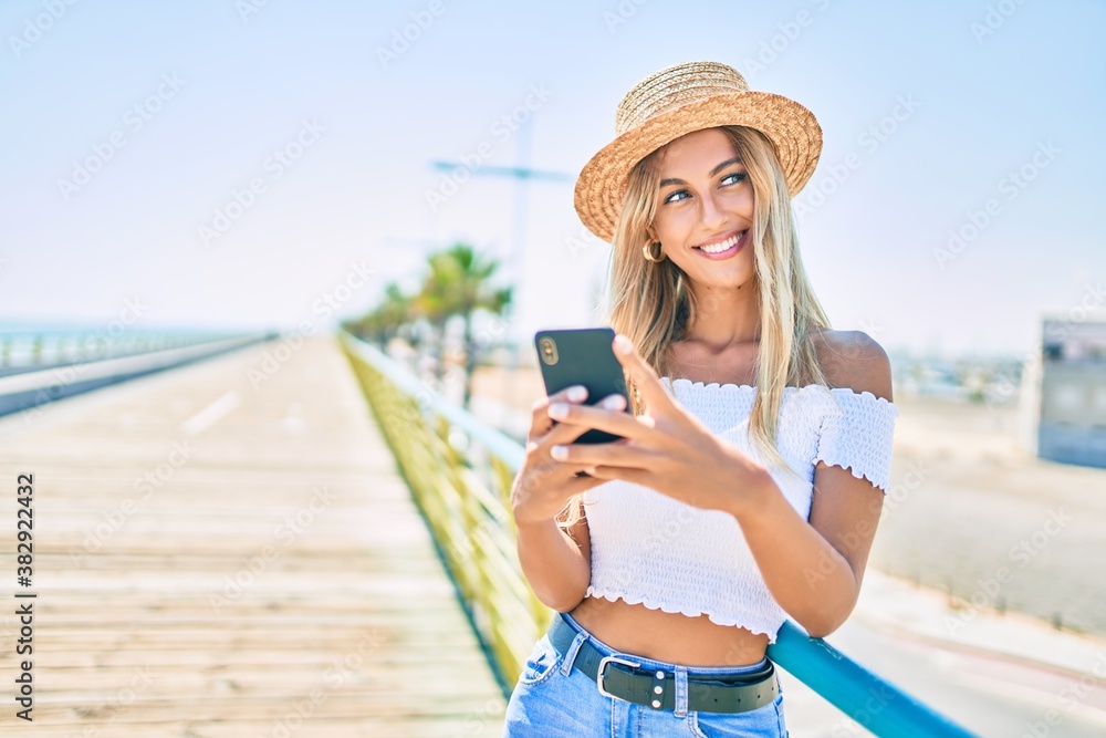 Young blonde tourist girl smiling happy using smartphone at the promenade.