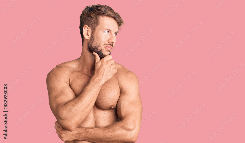 Fototapeta premium Young caucasian man standing shirtless with hand on chin thinking about question, pensive expression. smiling with thoughtful face. doubt concept.