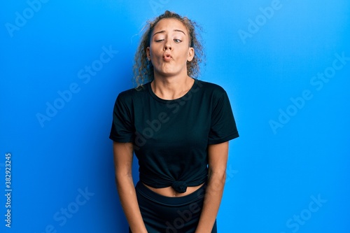 Fototapeta Beautiful caucasian teenager girl wearing black sportswear making fish face with lips, crazy and comical gesture