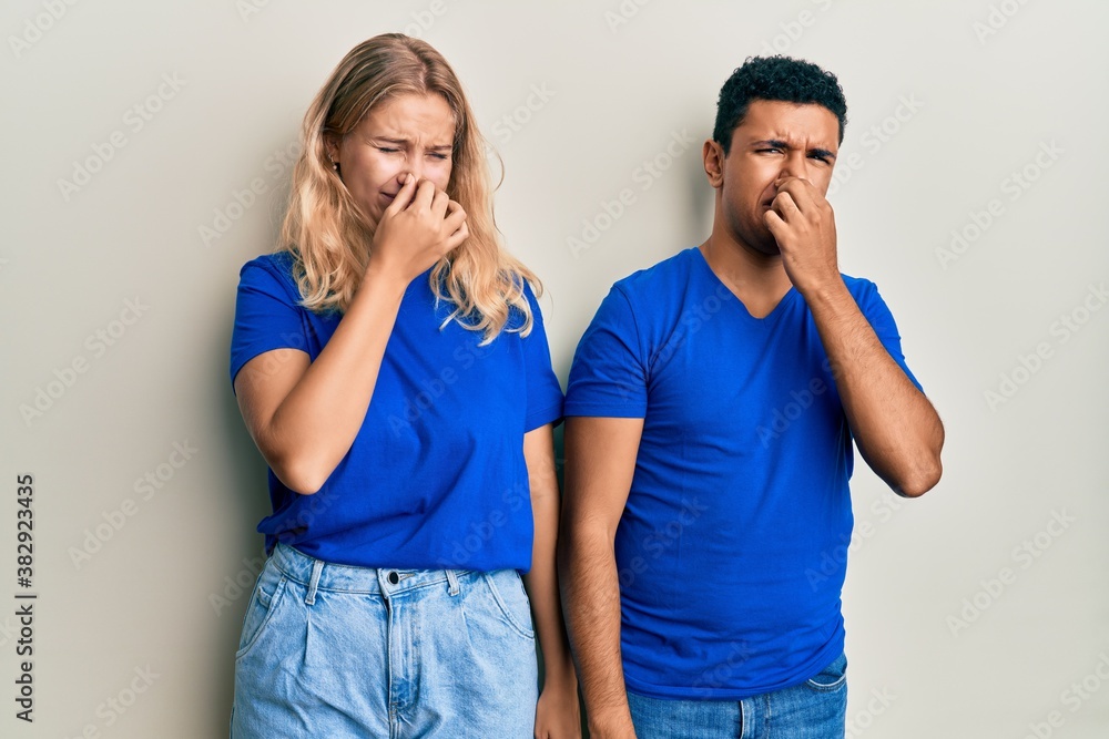 Young interracial couple wearing casual clothes smelling something stinky and disgusting, intolerable smell, holding breath with fingers on nose. bad smell Young interracial couple wearing casual clothes smelling something stinky and disgusting, intolerable smell, holding breath with fingers on nose. bad smell