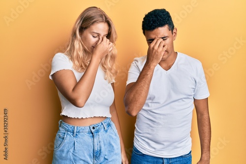 Young interracial couple wearing casual white tshirt tired rubbing nose and eyes feeling fatigue and headache. stress and frustration concept.