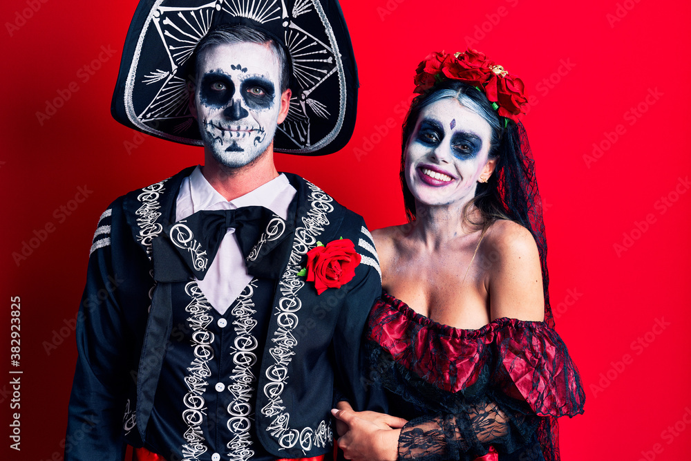 Young couple wearing mexican day of the dead costume over red with a happy and cool smile on face. lucky person. Young couple wearing mexican day of the dead costume over red with a happy and cool smile on face. lucky person.