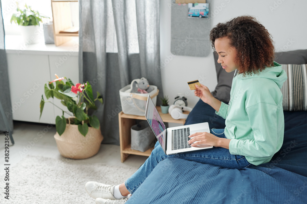 Happy mixed-race girl sitting on bed and going to do shopping in online shop Happy mixed-race girl sitting on bed and going to do shopping in online shop