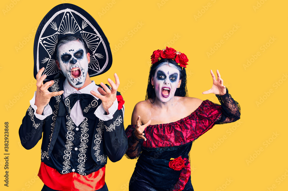 Young couple wearing mexican day of the dead costume over background shouting frustrated with rage, hands trying to strangle, yelling mad