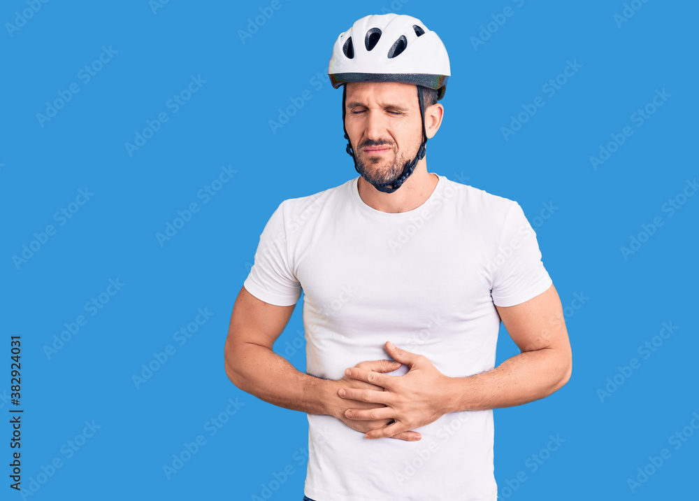 Young handsome man wearing bike helmet with hand on stomach because indigestion, painful illness feeling unwell. ache concept. Young handsome man wearing bike helmet with hand on stomach because indigestion, painful illness feeling unwell. ache concept.