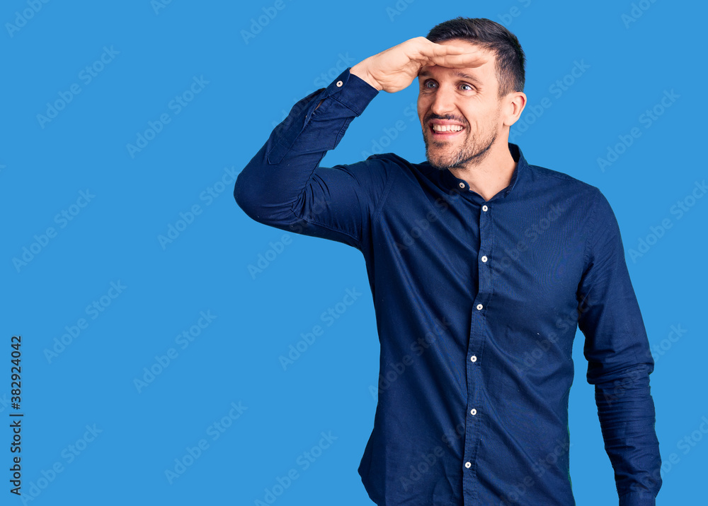 Young handsome man wearing casual shirt very happy and smiling looking far away with hand over head. searching concept. Young handsome man wearing casual shirt very happy and smiling looking far away with hand over head. searching concept.