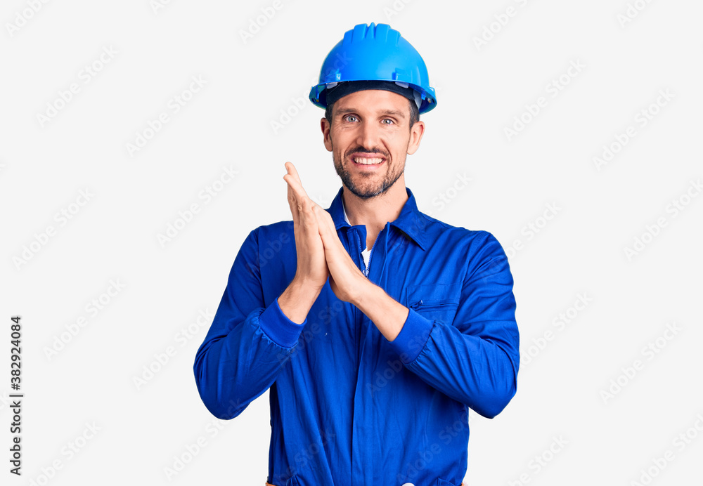 Young handsome man wearing worker uniform and hardhat clapping and applauding happy and joyful, smiling proud hands together