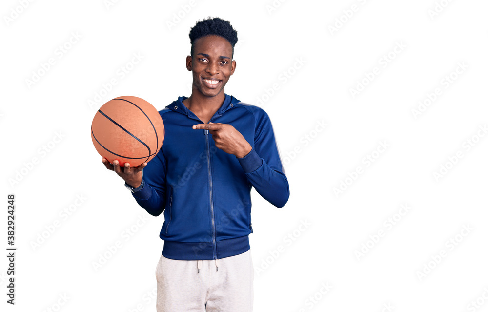 Young african american man holding basketball ball smiling happy pointing with hand and finger