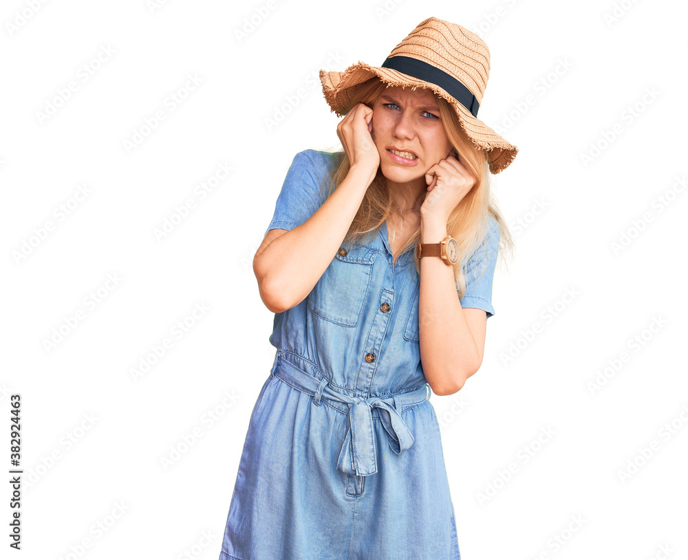 Young beautiful blonde woman wearing summer hat and dress covering ears with fingers with annoyed expression for the noise of loud music. deaf concept. Young beautiful blonde woman wearing summer hat and dress covering ears with fingers with annoyed expression for the noise of loud music. deaf concept.