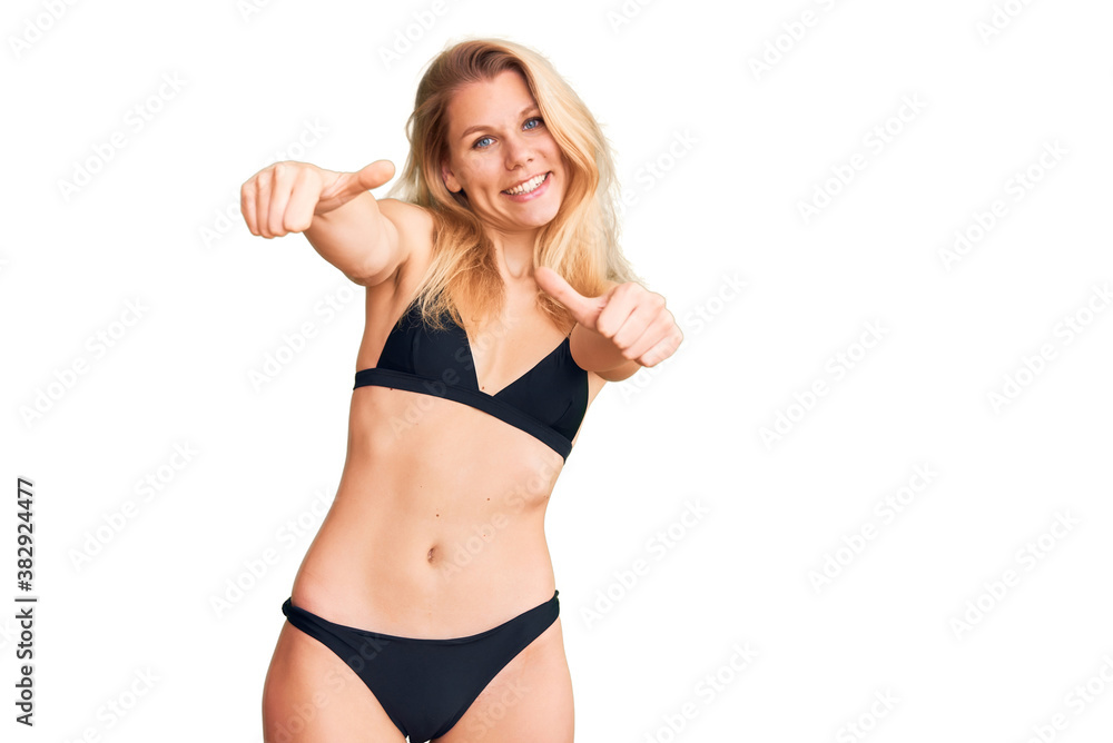Young beautiful blonde woman wearing bikini approving doing positive gesture with hand, thumbs up smiling and happy for success. winner gesture. Young beautiful blonde woman wearing bikini approving doing positive gesture with hand, thumbs up smiling and happy for success. winner gesture.