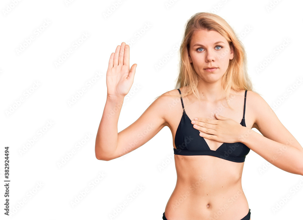 Young beautiful blonde woman wearing bikini swearing with hand on chest and open palm, making a loyalty promise oath Young beautiful blonde woman wearing bikini swearing with hand on chest and open palm, making a loyalty promise oath