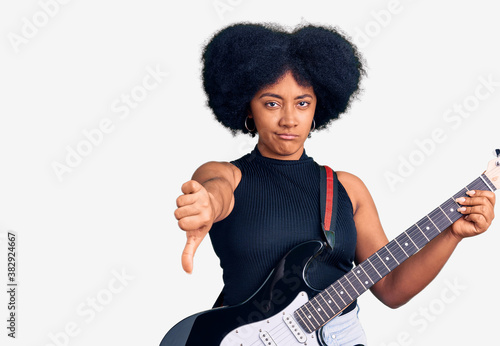 Young african american girl playing electric guitar with angry face, negative sign showing dislike with thumbs down, rejection concept