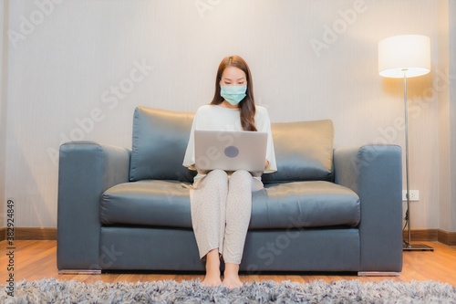 Portrait beautiful young asian woman wear mask and use computer laptop on sofa