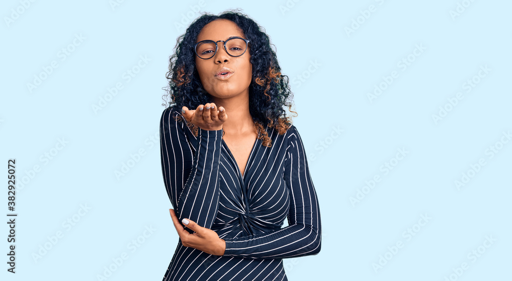 Young african american woman wearing casual clothes and glasses looking at the camera blowing a kiss with hand on air being lovely and sexy. love expression. Young african american woman wearing casual clothes and glasses looking at the camera blowing a kiss with hand on air being lovely and sexy. love expression.