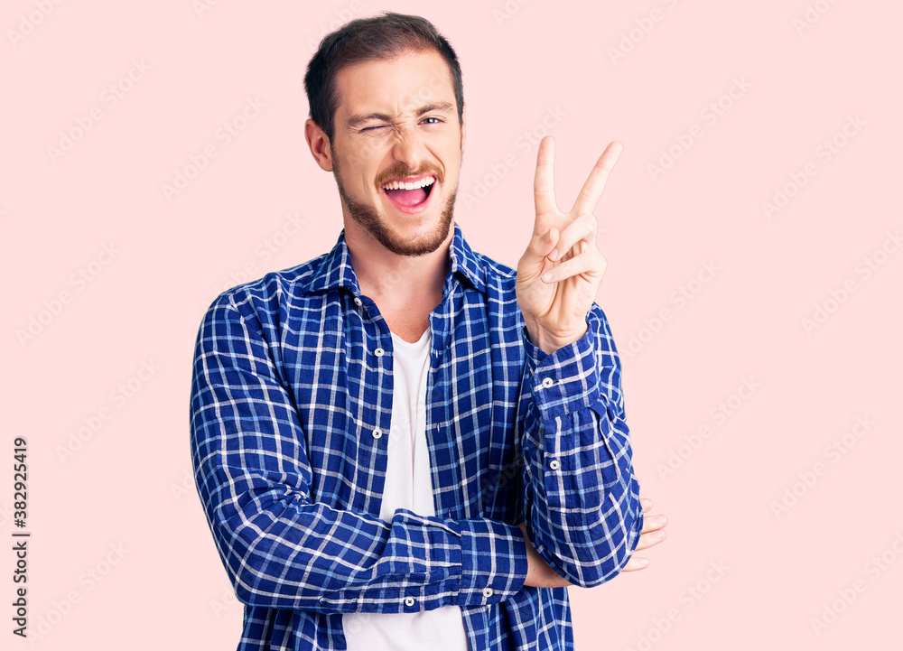 Young handsome caucasian man wearing casual clothes smiling with happy face winking at the camera doing victory sign. number two. Young handsome caucasian man wearing casual clothes smiling with happy face winking at the camera doing victory sign. number two.