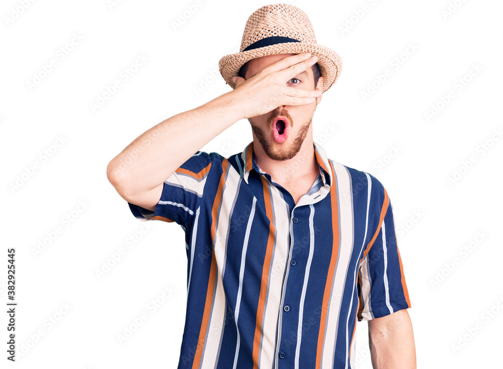 Young handsome caucasian man wearing summer hat peeking in shock covering face and eyes with hand, looking through fingers with embarrassed expression. Young handsome caucasian man wearing summer hat peeking in shock covering face and eyes with hand, looking through fingers with embarrassed expression.