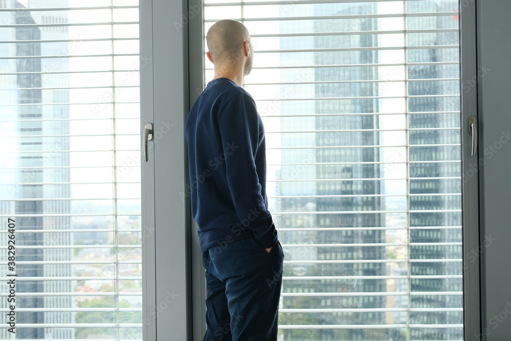 Fototapeta premium young man stands in an office in front of a window, looks at a modern European city, the concept of a business idea, a workplace