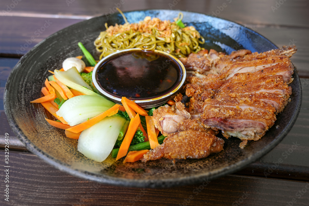 Fototapeta premium Asian dish with roasted duck, vegetables, noodles and teriyaki sauce in a flat bowl on a wooden table, selected focus