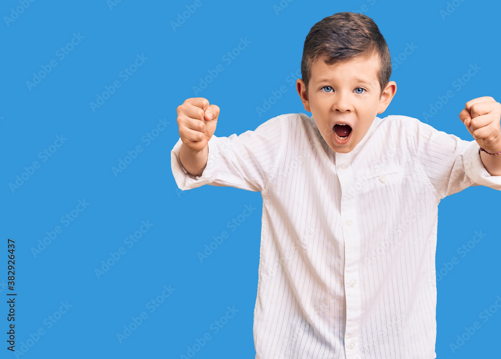 Cute blond kid wearing elegant shirt angry and mad raising fists frustrated and furious while shouting with anger. rage and aggressive concept. Cute blond kid wearing elegant shirt angry and mad raising fists frustrated and furious while shouting with anger. rage and aggressive concept.