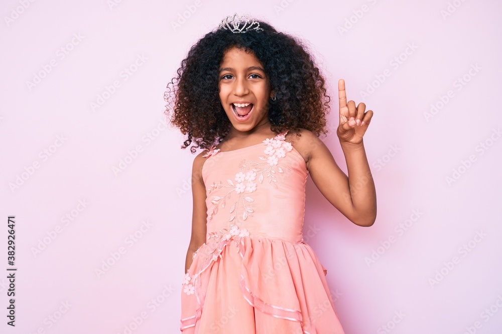 African american child with curly hair wearing princess crown smiling with an idea or question pointing finger up with happy face, number one African american child with curly hair wearing princess crown smiling with an idea or question pointing finger up with happy face, number one