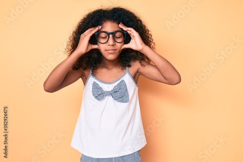 African american child with curly hair wearing casual clothes and glasses with hand on head, headache because stress. suffering migraine.