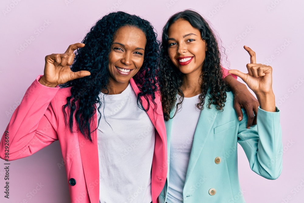African american mother and daughter wearing business style smiling and confident gesturing with hand doing small size sign with fingers looking and the camera. measure concept. African american mother and daughter wearing business style smiling and confident gesturing with hand doing small size sign with fingers looking and the camera. measure concept.