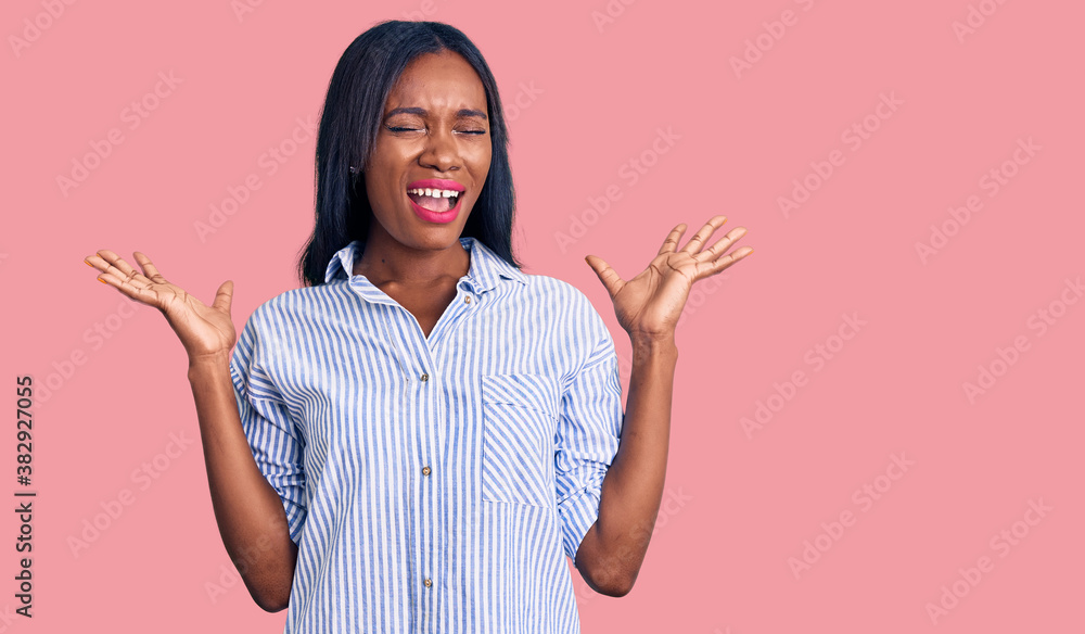 Young african american woman wearing casual clothes celebrating mad and crazy for success with arms raised and closed eyes screaming excited. winner concept Young african american woman wearing casual clothes celebrating mad and crazy for success with arms raised and closed eyes screaming excited. winner concept