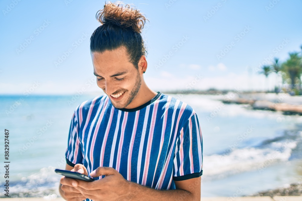 Young hispanic man smiling happy using smartphone at the beach. Young hispanic man smiling happy using smartphone at the beach.