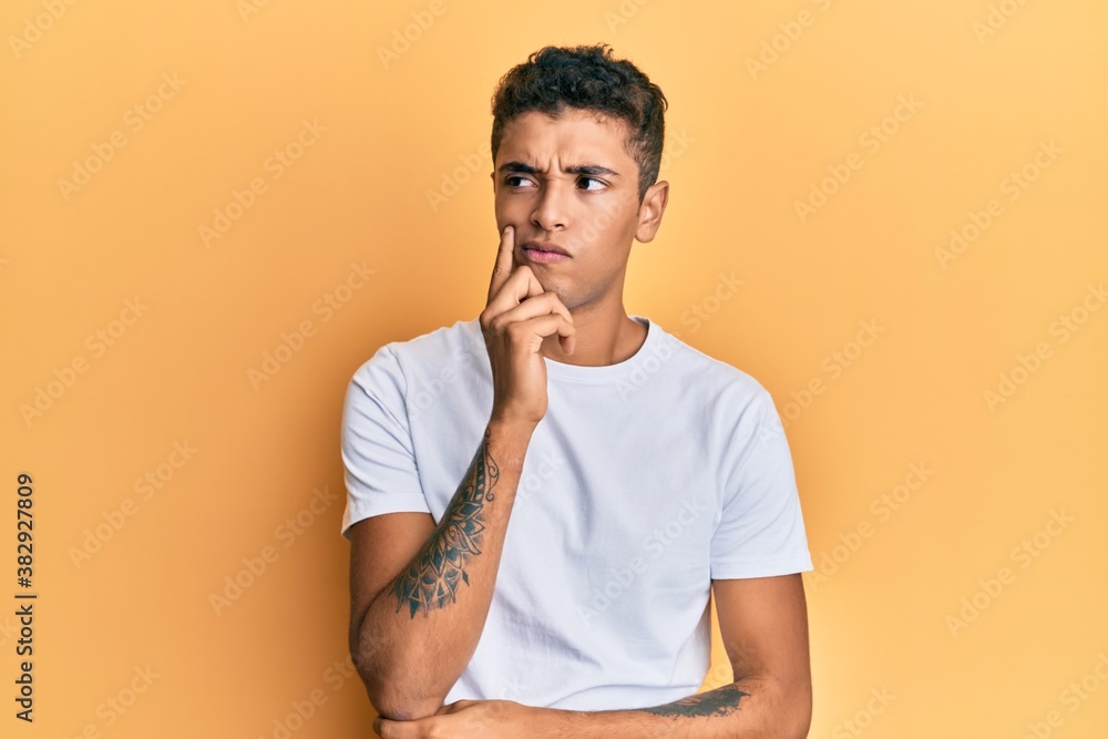 Young handsome african american man wearing casual white tshirt serious face thinking about question with hand on chin, thoughtful about confusing idea Young handsome african american man wearing casual white tshirt serious face thinking about question with hand on chin, thoughtful about confusing idea