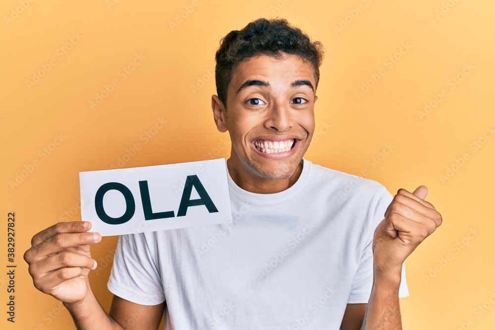 Young handsome african american man holding ola as portuguese greeting screaming proud, celebrating victory and success very excited with raised arm Young handsome african american man holding ola as portuguese greeting screaming proud, celebrating victory and success very excited with raised arm