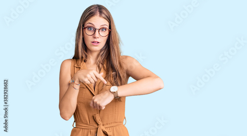 Young beautiful blonde woman wearing casual clothes and glasses in hurry pointing to watch time, impatience, upset and angry for deadline delay