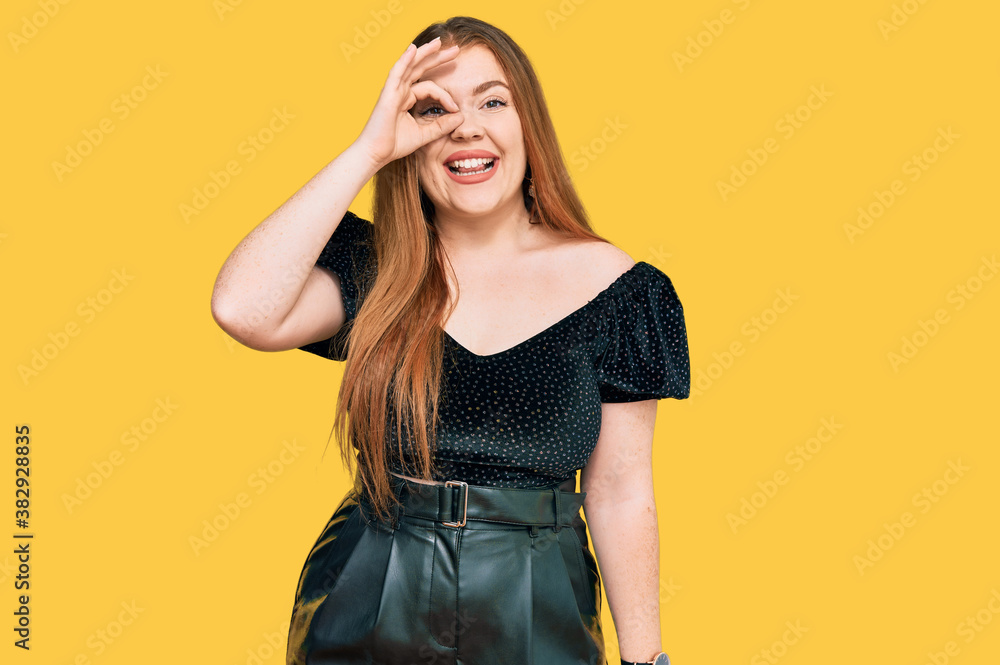 Young beautiful redhead woman wearing elegant clothes doing ok gesture with hand smiling, eye looking through fingers with happy face. Young beautiful redhead woman wearing elegant clothes doing ok gesture with hand smiling, eye looking through fingers with happy face.