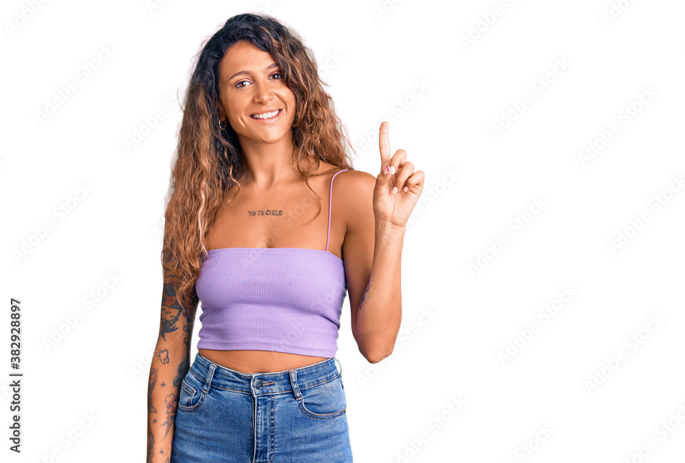 Young hispanic woman with tattoo wearing casual clothes showing and pointing up with finger number one while smiling confident and happy. Young hispanic woman with tattoo wearing casual clothes showing and pointing up with finger number one while smiling confident and happy.