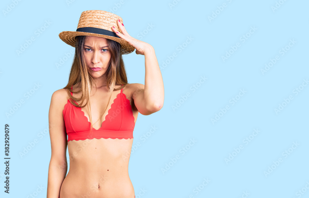 Beautiful brunette young woman wearing bikini confuse and wonder about question. uncertain with doubt, thinking with hand on head. pensive concept.