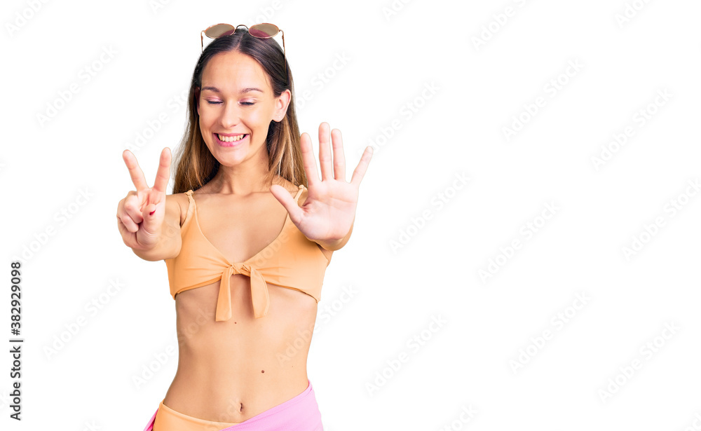 Beautiful brunette young woman wearing bikini and sunglasses showing and pointing up with fingers number seven while smiling confident and happy. Beautiful brunette young woman wearing bikini and sunglasses showing and pointing up with fingers number seven while smiling confident and happy.